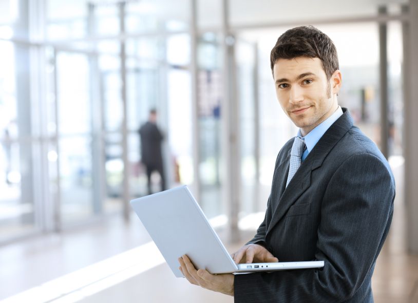 Young smiling businessman using laptop on corporate location, indoor.
